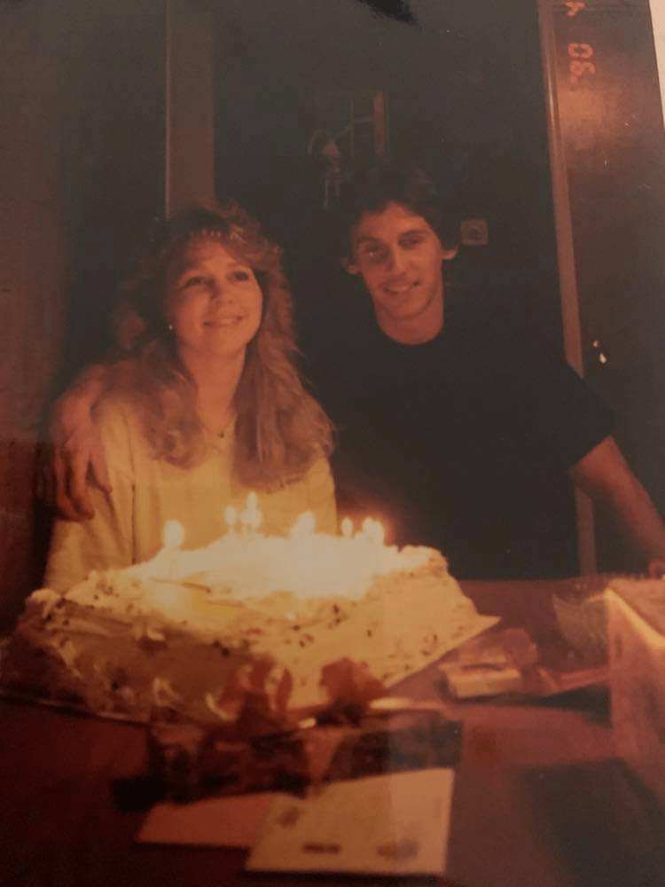 Dani and Dennis seated at a table with a large cake with lighted candles - vintage photo of the young couple