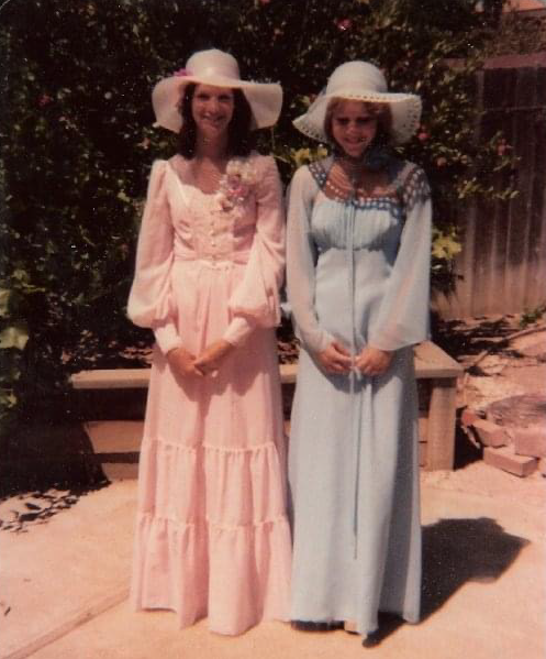 Two young women in old fashioned pastel color long dresses and wide brim hats