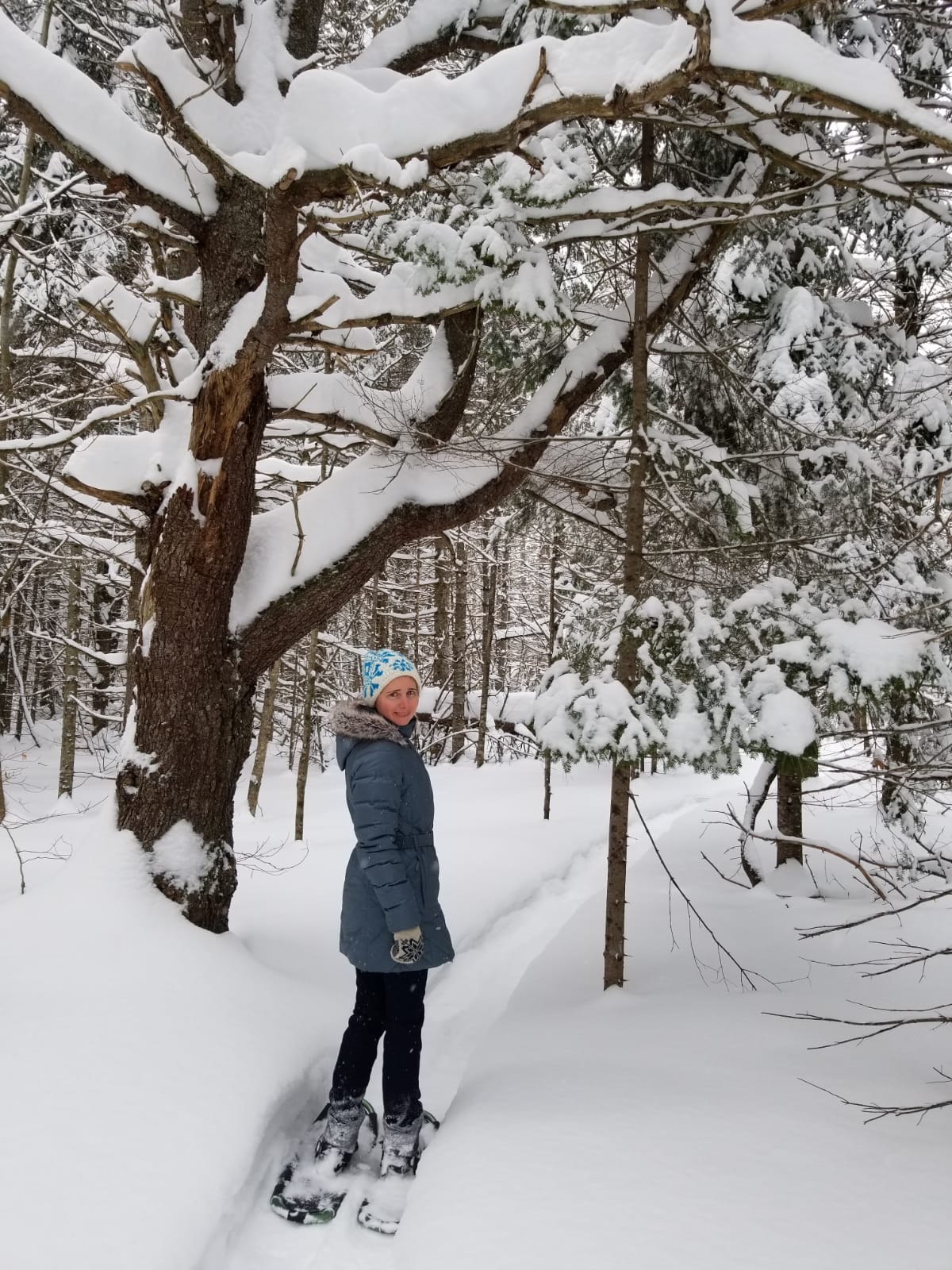 Elena on snow shoes on a trail through snowy trees. 