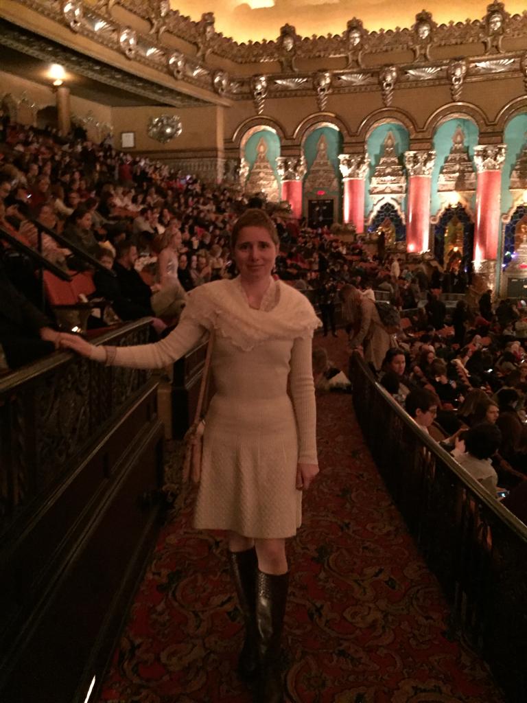 Elena, in winter white knt dress at a formal ornate theater