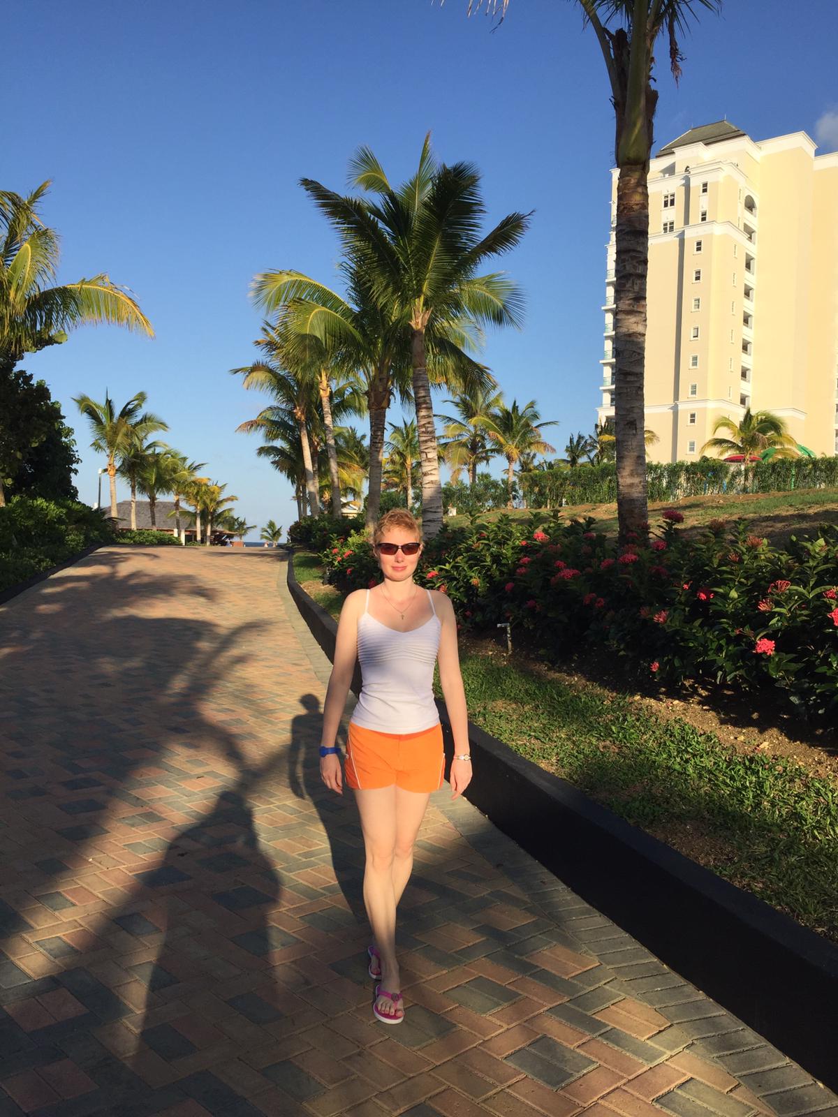 Elena in shorts and sun top on a palm tree lined brick walkway