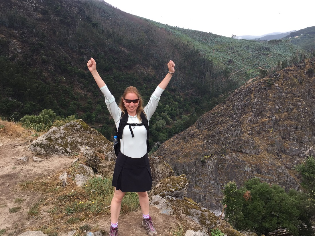  Elena in hiking gear with arms raised in victory atop a mountain